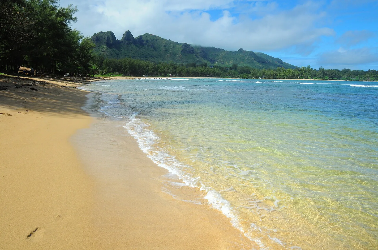 Anahola Bay's golden crescent beach and clear water under the jagged Kalalea ridge.