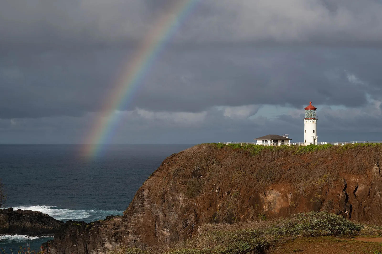 The Daniel K. Inouye Lighthouse at Kīlauea Point with a rainbow arcing over the ocean.
